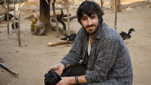 Skuespilleren Eoin Macken sitter på en benk og smiler.