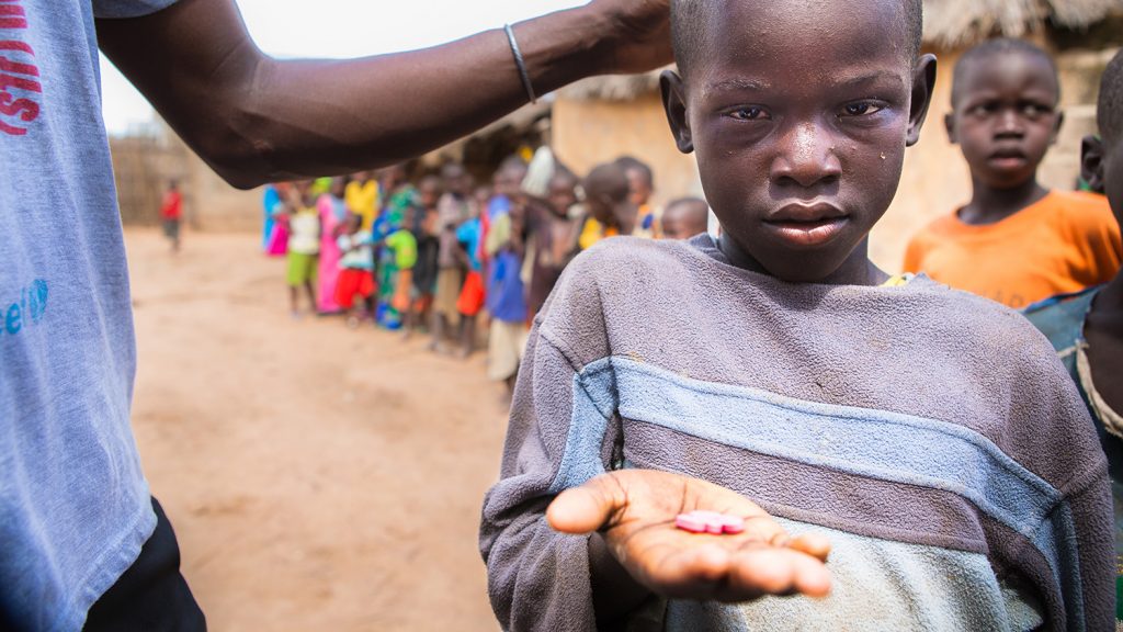 En ung gutt holder hånden sin opp mot kameraet, og viser frem trakom-medisinene han holder.