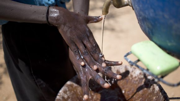 Nærbilde av et barn som vasker hendene sine under en vannkran.