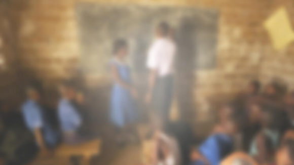 Et uklart bilde av et klasserom i Sierra Leone. Bildet er utydelig og uskarpt med et hvitaktig skjær. Det er vankelig å se læreren og tavla klart.