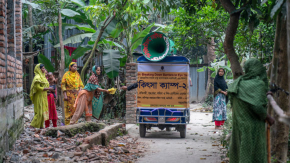 A tuk tuk passes a group of women.