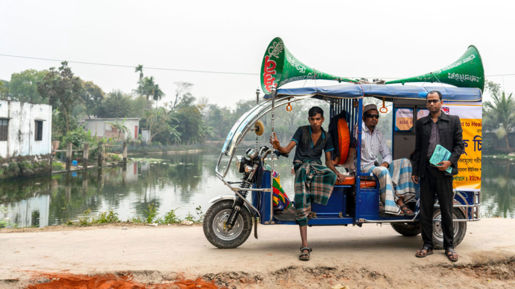 En fargerik tuk-tuk taxi med en megafon på taket og tre menn stående ved siden.