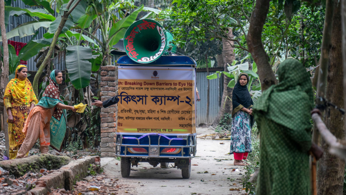 En tuk-tuk passerer en gruppe kvinner.