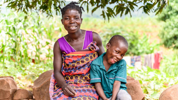 Taonga og moren hans sitter ute. De smiler og er glade.