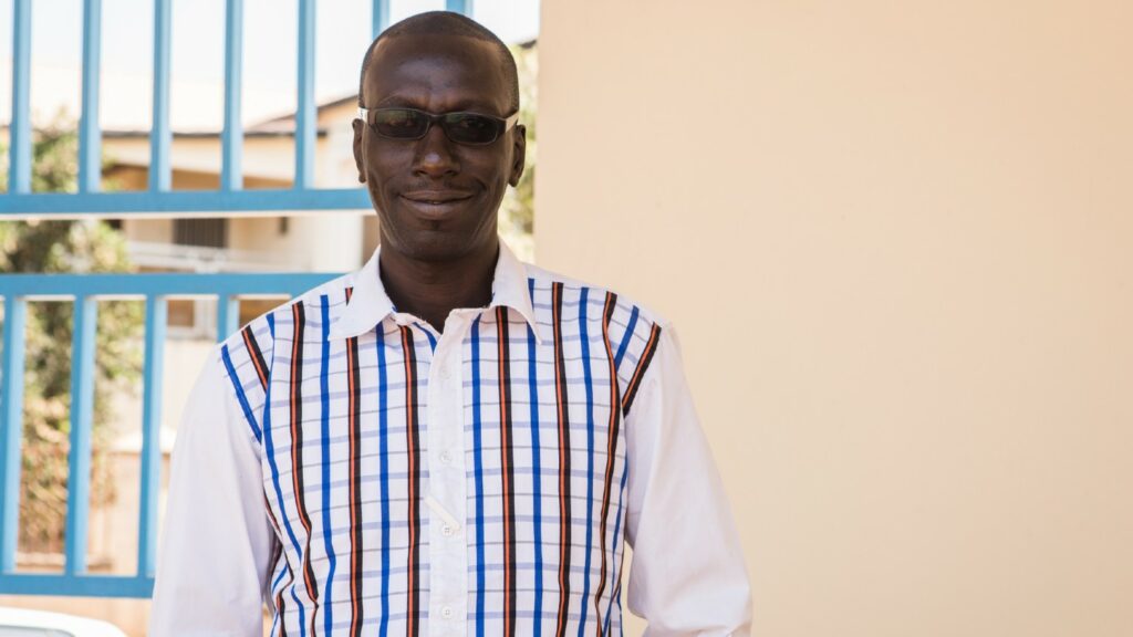 Sarjo Kanyj, lokal leder for prosjektet Nasjonal øyehelse, står utenfor en bygning.