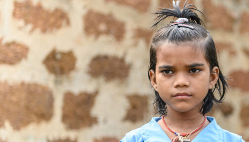 Archana stands in front of a brick wall, looking just off camera into the distance.