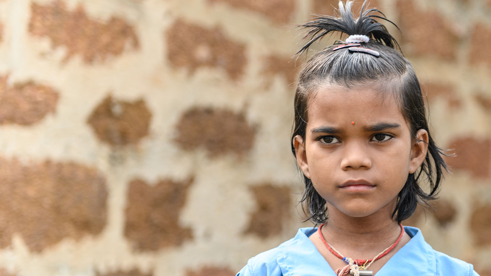 Archana stands in front of a brick wall, looking just off camera into the distance.