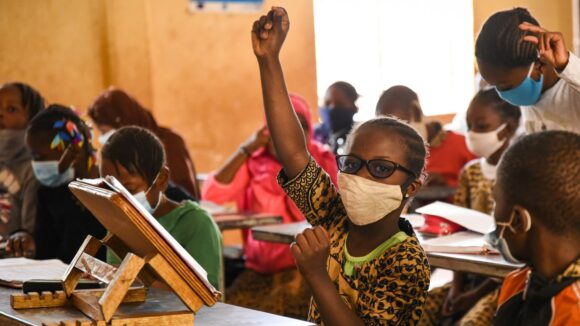 A young girl raising her hand in a classroom.