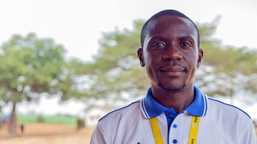 Ndelle Makoge har et Sightsavers-skilt på seg og står utendørs i Kamerun.