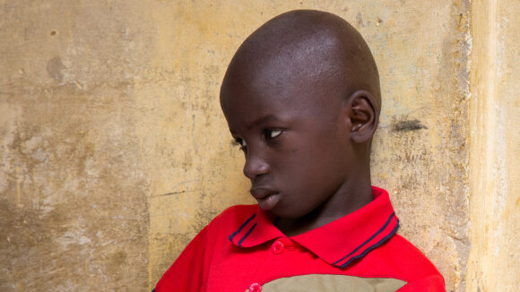 Souleymane leans against a wall and chair in his home.