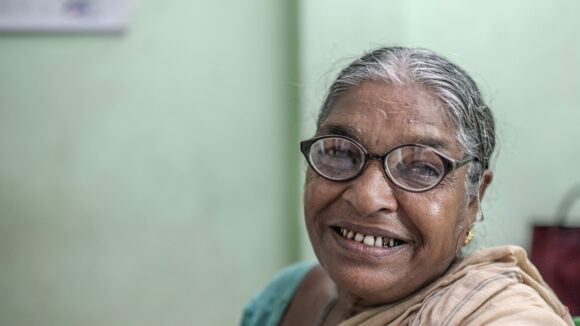 Monimala, en eldre kvinne fra India, smiler mens hun har på seg brillene.