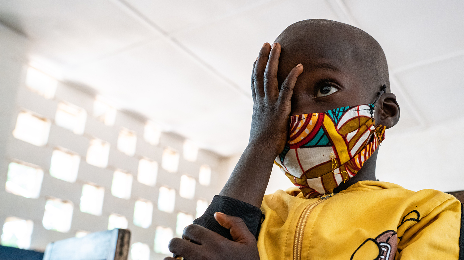 En gutt med en fargesterk maske holder en hånd over det ene øyet under en synsprøve.