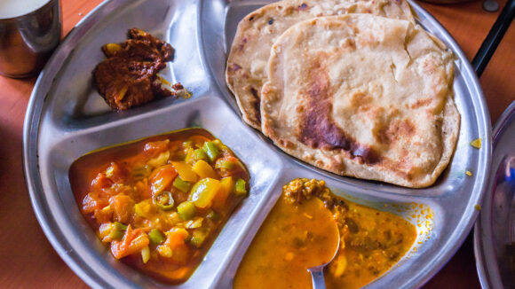 En metalltallerken full av indisk mat.