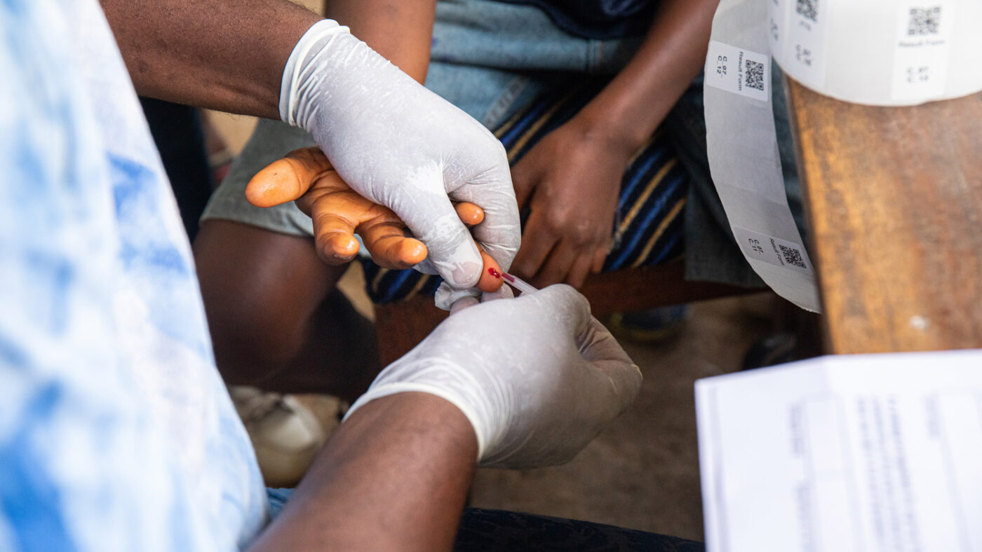 En helsearbeider iført operasjonshansker tar en blodprøve fra en skoleelev.