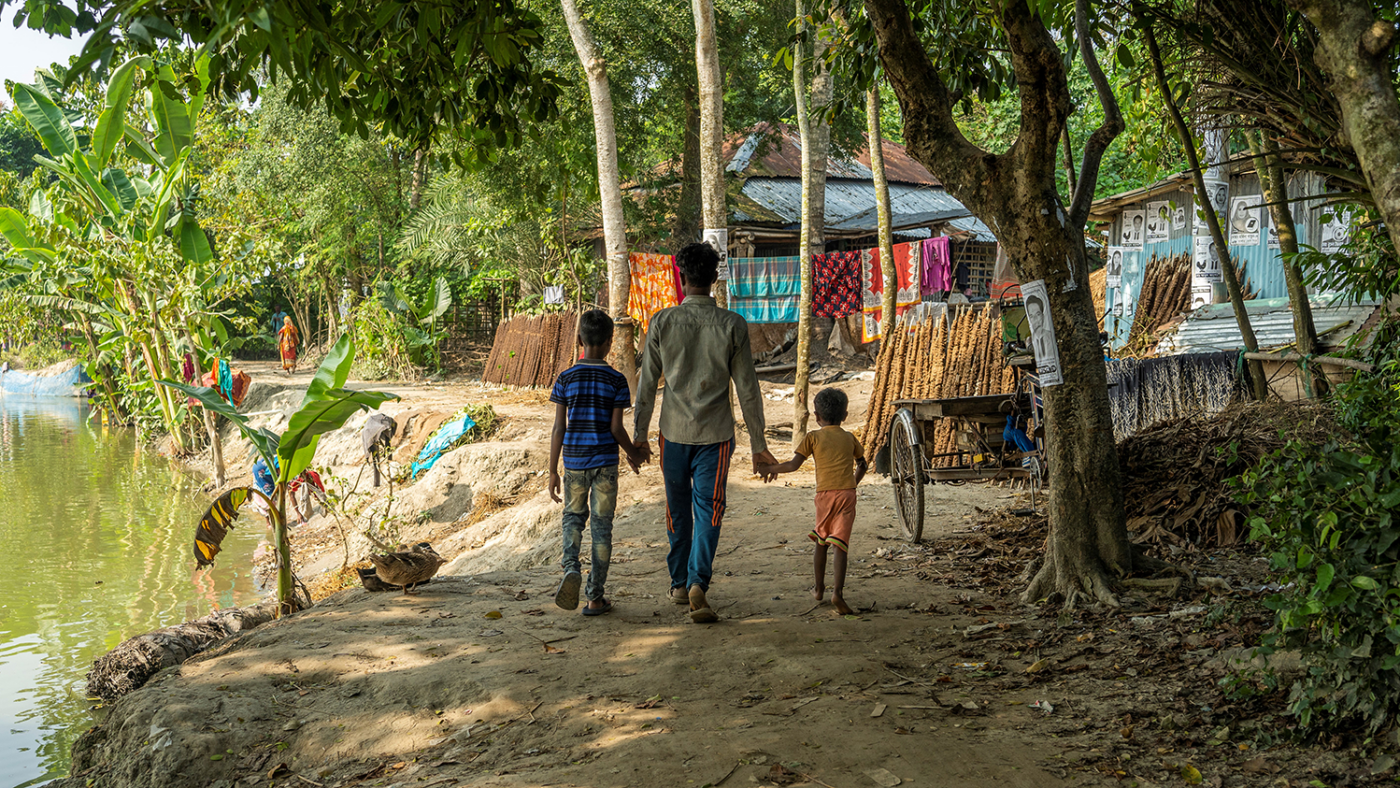 A man walks away from the camera holding the hands of his two small children.