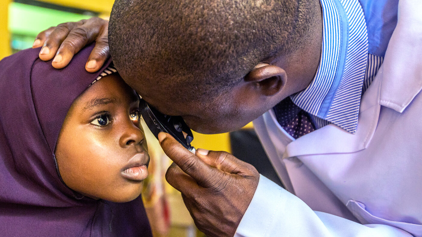 En ung jente iført et lilla skaut har øynene undersøkt av en øyelege iført en hvit frakk.