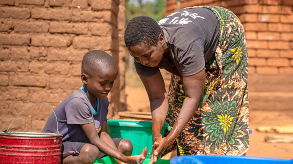 Rose og hennes barnebarn Jonathan utenfor hjemmet deres i Malawi. De ser på hverandre og smiler.