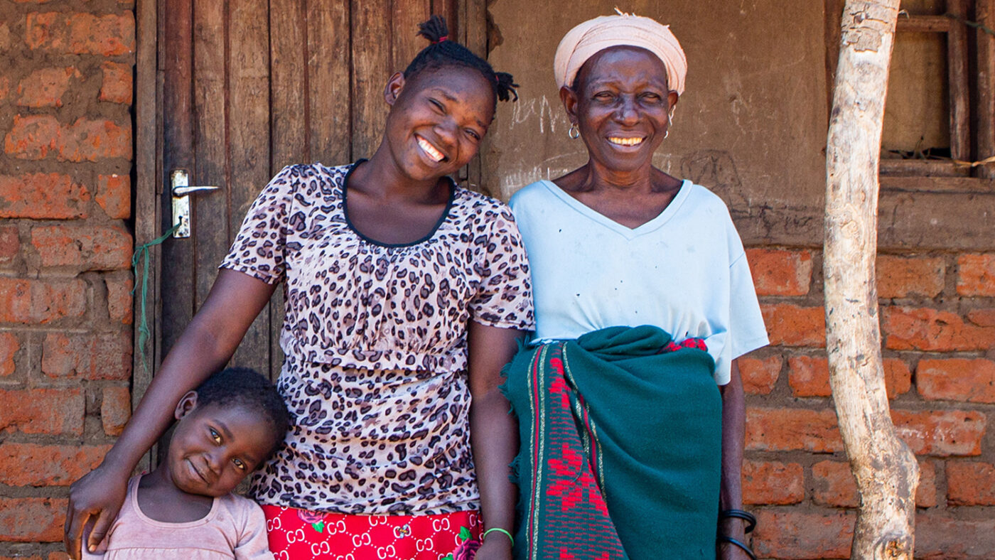 Achiwa står sammen med barnebarnet og oldebarnet utenfor hjemmet deres.