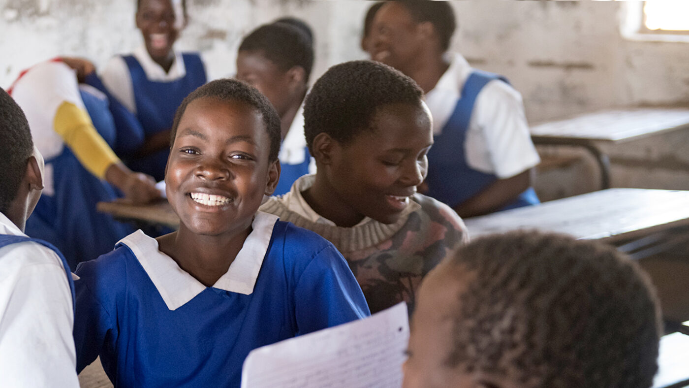 Skoleelever i et klasserom i Malawi, iført knallblå uniformer. Man smiler bredt til kamera.