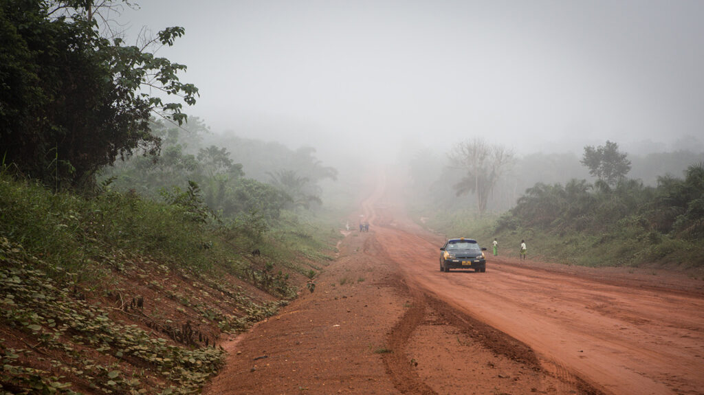 En bil kjører langs en bred, støvete vei i det landlige Ghana.