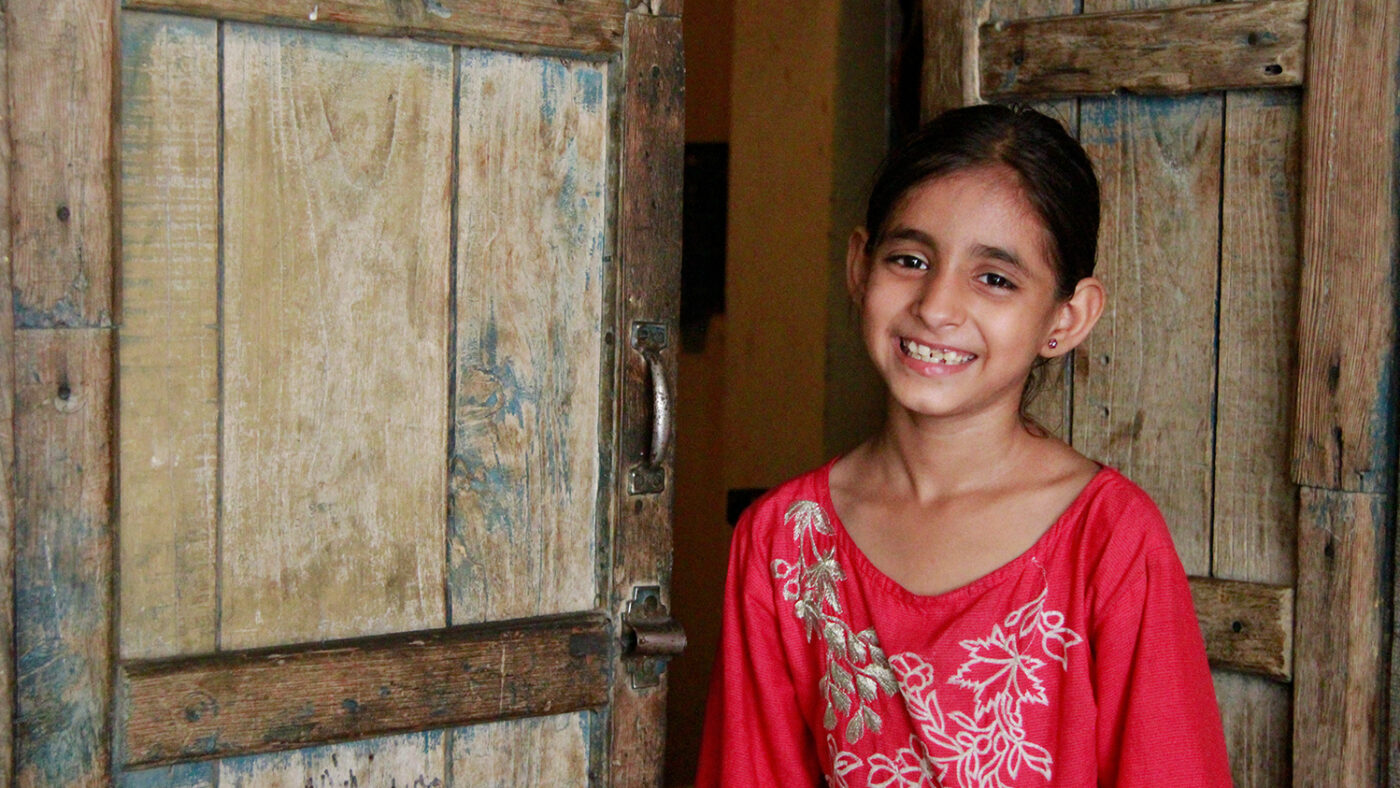 Ni år gamle Nayab smiler utenfor hjemmet sitt i Pakistan.