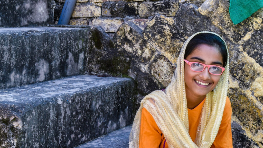 Aakasha sits outside sitting on a step and smiles at the camera.
