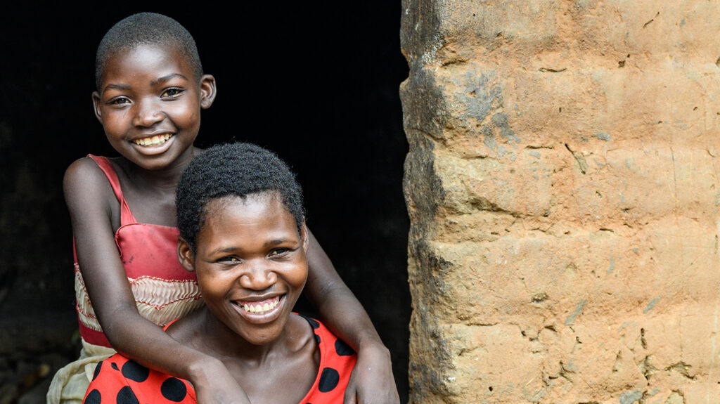 En ung jente som smiler med armene viklet rundt moren.