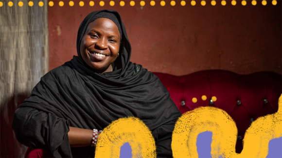 En kvinne iført en svart chador (tradisjonell kappe) smiler mens hun sitter i en sofa.