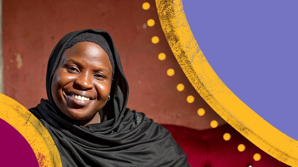 En kvinne iført en svart chador (tradisjonell kappe) smiler mens hun sitter i en sofa.