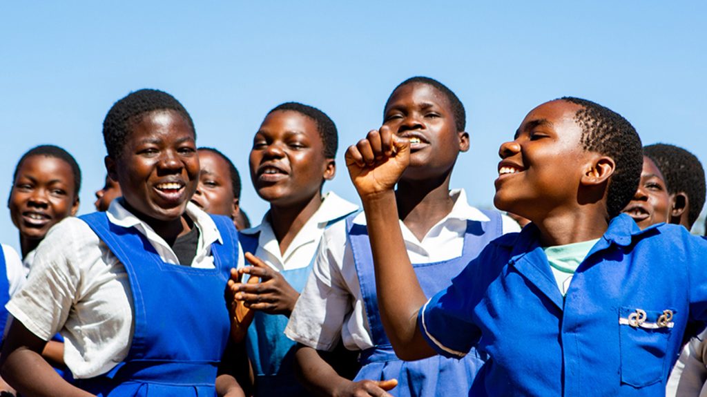 En gruppe tenåringsjenter i skoleuniform jubler og vifter med armene i været.