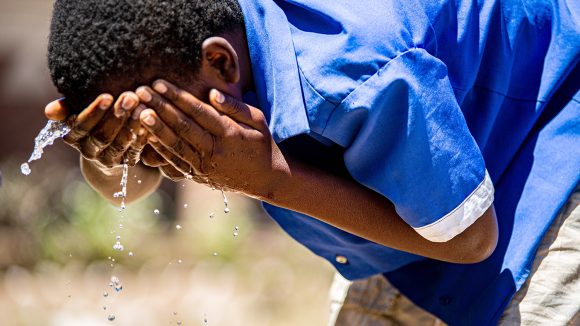 Et barn vasker ansiktet sitt med vann.