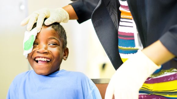 En ung jente smiler bredt idet bandasjen hennes fjernes etter grå stær-operasjon.