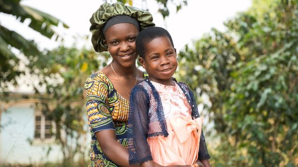Samantha står utendørs med moren sin. De smiler begge til kameraet.