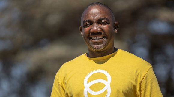 Restman wears a yellow Sightsavers t-shirt and smiles at the camera.