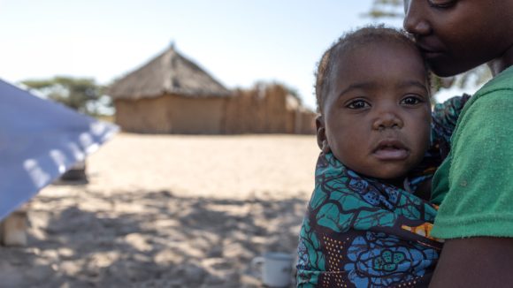 17-month-old Sarah, who is being held by her mother Lupula, looks at the camera.