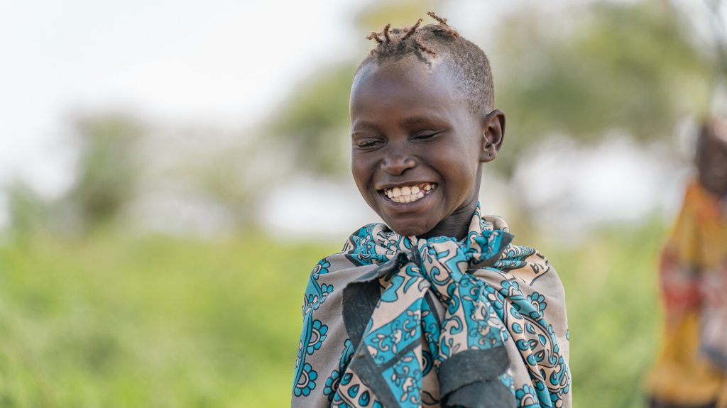 Namoite sitter ute og smiler mens hun lager dekorative perler i Kenya.